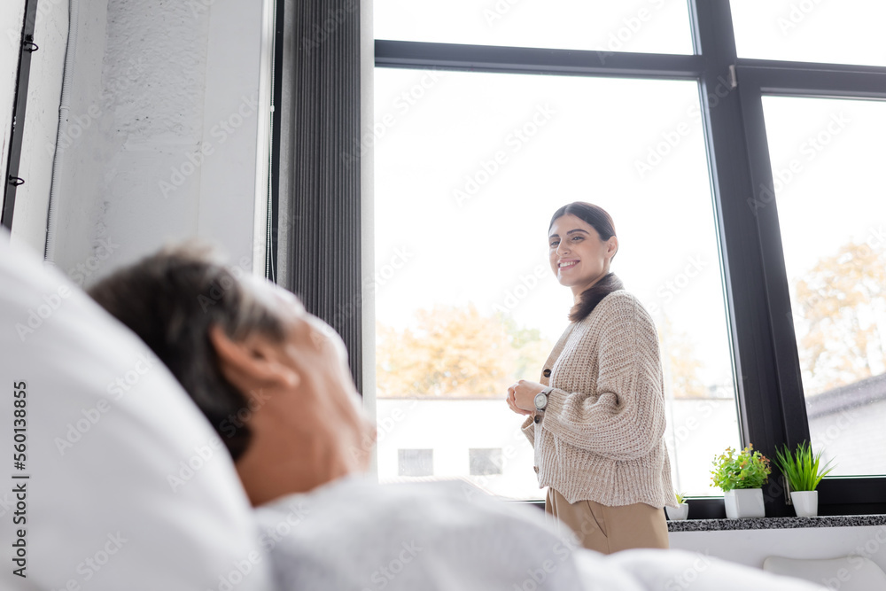 Smiling woman looking at blurred father lying on hospital bed. Smiling woman looking at blurred father lying on hospital bed.