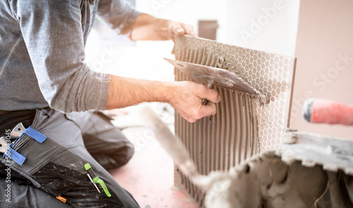 Fliesenleger trägt mit der Zahnkelle den Fliesenkleber auf die Fliese auf