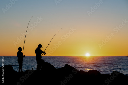 Beautiful sunset over the ocean with two men fishing