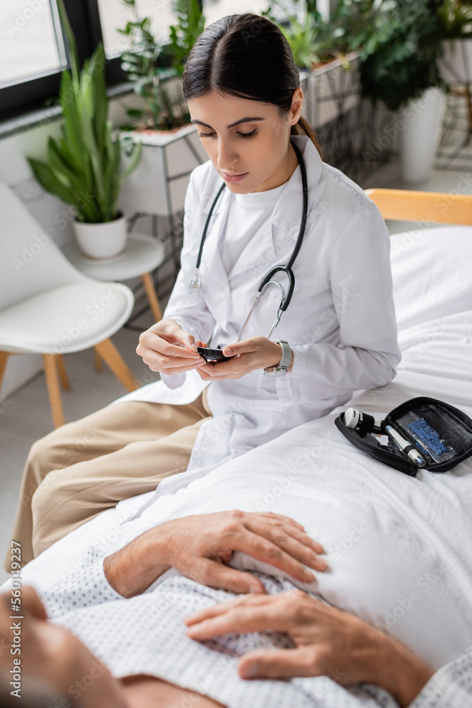 Obraz premium Doctor holding glucometer near senior patient on bed in clinic.