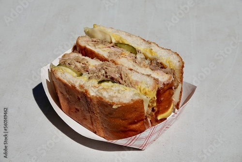 A delicious Cuban sandwich with pulled pork, pickles, cheese and sauce on a paper plate. Authentic street food from a food truck. High quality photo