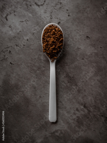 One spoonful of instant granulated coffee isolated on a dark kitchen counter. Top view flat lay with vertical orientation