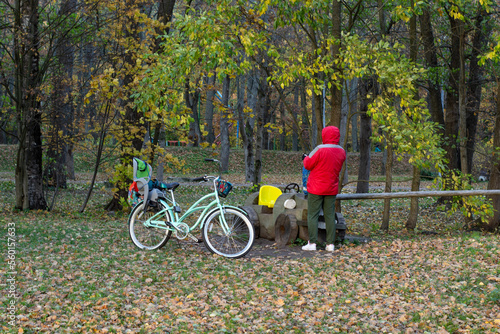 A man in a red jacket walks in an autumn park, next to a bicycle with a child seat