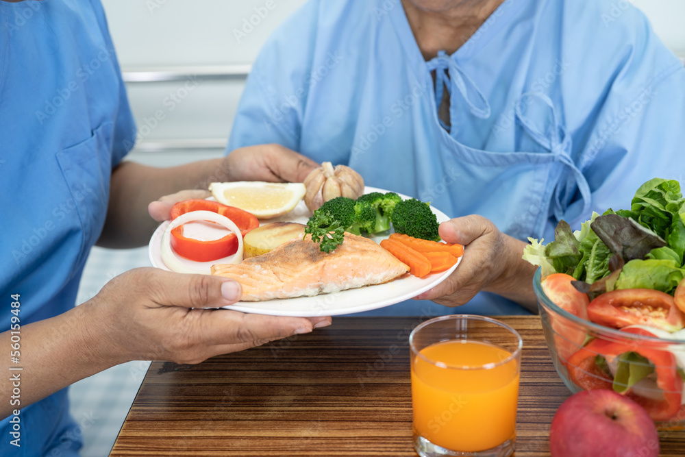 Asian senior or elderly old lady woman patient eating Salmon steak breakfast with vegetable healthy food while sitting and hungry on bed in hospital. Asian senior or elderly old lady woman patient eating Salmon steak breakfast with vegetable healthy food while sitting and hungry on bed in hospital.