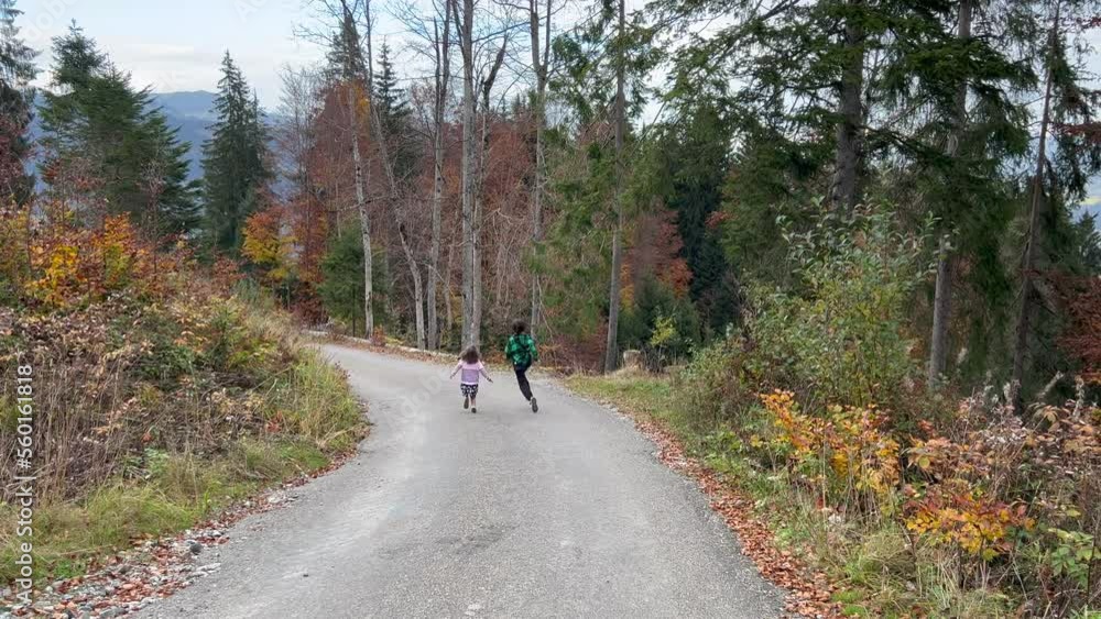 Brother and sister running through winding road amidst trees in forest Brother and sister running through winding road amidst trees in forest