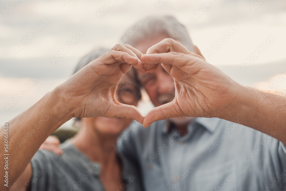 Close up portrait happy sincere middle aged elderly retired family couple making heart gesture with fingers, showing love or demonstrating sincere feelings together outdoors, looking at camera.. - obrazy, fototapety, plakaty 