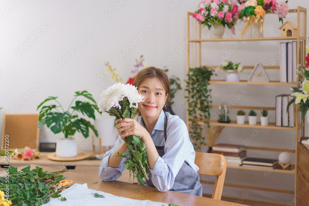Florist concept, Woman florist holding bunch of white chrysanthemum and smiling at flower shop Florist concept, Woman florist holding bunch of white chrysanthemum and smiling at flower shop