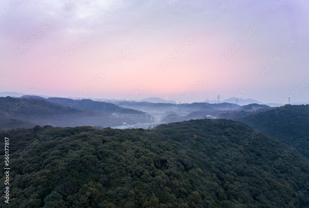Distant early morning sun lights sky pink over misty hilly landscape