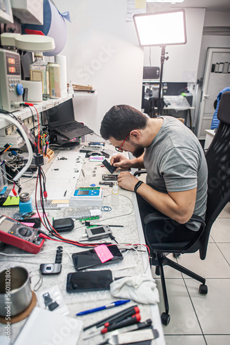 Electronics repair shop  a repairman is surrounded by tools and equipment. A technician repairs  cleans  controls a smartphone. Workplace top view  close-up.