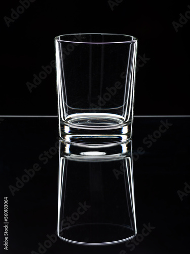 A glass tumbler on a glass shelf with a contrasting mirror image. Outline illumination. Black background. The vertical position of the frame. Free space for text advertising