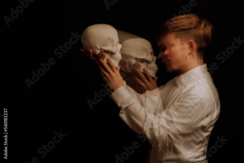 woman is a psychopath with schizophrenia and mental disorders. Portrait of a paranoid girl with a skull in her hands on a dark background