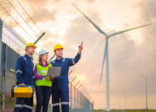 Technician engineer in uniform with standing and checking wind turbine power farm power generator Station. Clean energy and environment. Young maintenance engineer team working in wind turbine farm