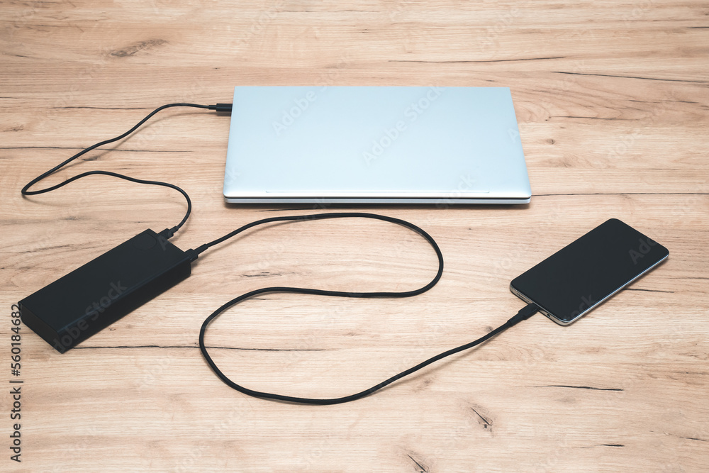 Power bank with usb-c cable is charging laptop and smartphone. Modern, information technology. Power bank with usb-c cable is charging laptop and smartphone. Modern, information technology.