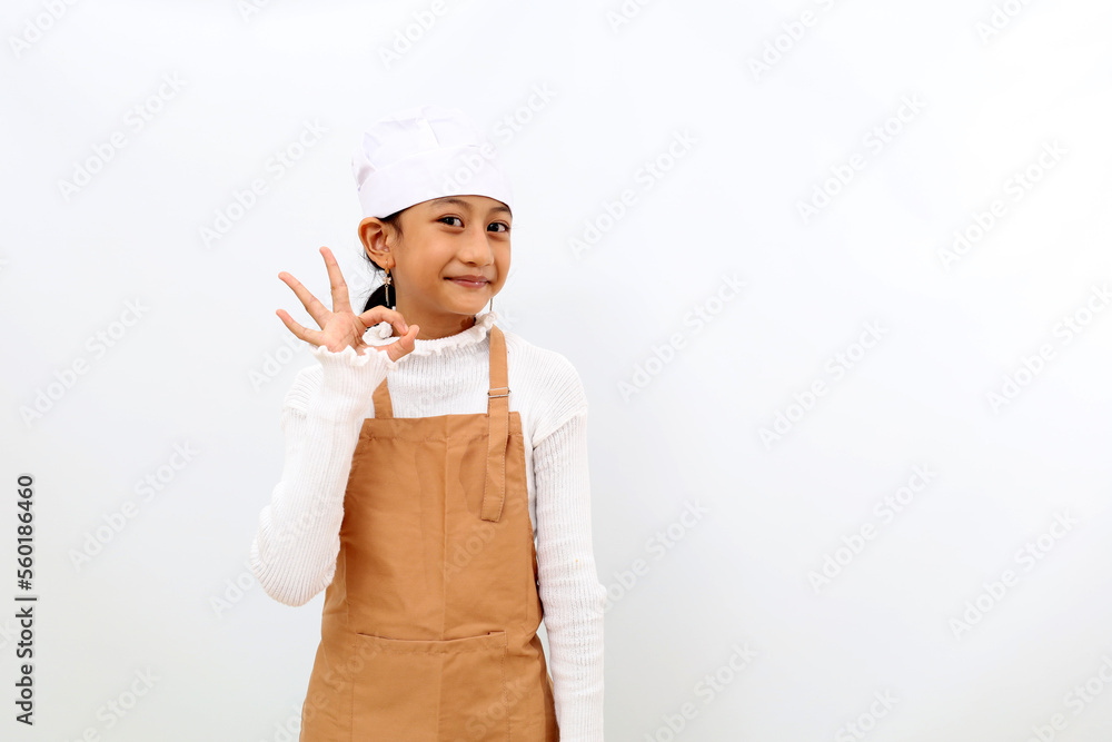 Happy little girl in chef uniform making okay hand gesture. Isolated on white background Happy little girl in chef uniform making okay hand gesture. Isolated on white background