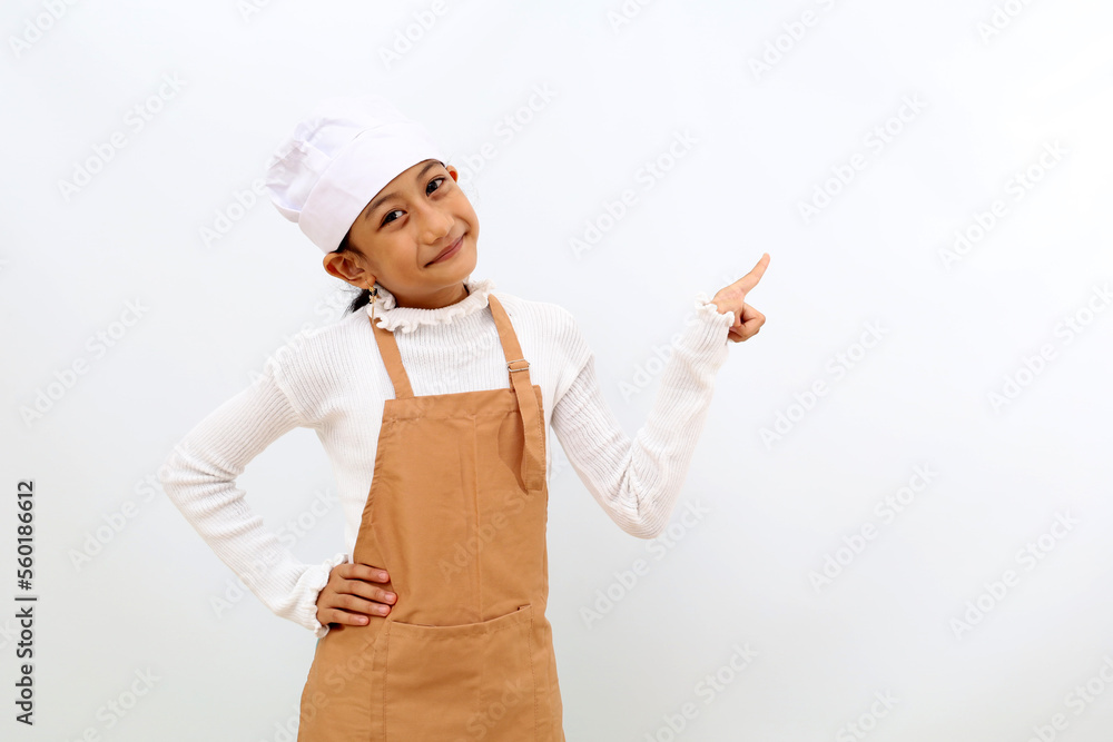 Cheerful little girl in chef uniform presenting something at blank space. Isolated on white background Cheerful little girl in chef uniform presenting something at blank space. Isolated on white background