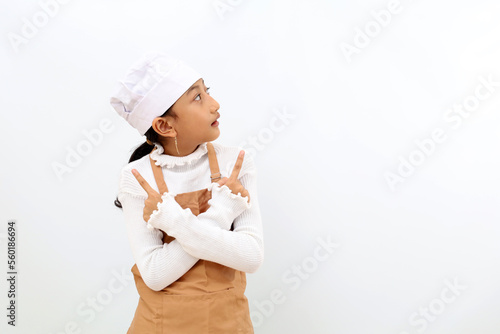 Happy little girl in chef uniform pointing both sides and looking at empty space. Isolated on white background