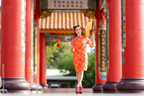 Asian woman in red cheongsam qipao dress holding paper fan while visiting the Chinese Buddhist temple during lunar new year for traditional culture concept