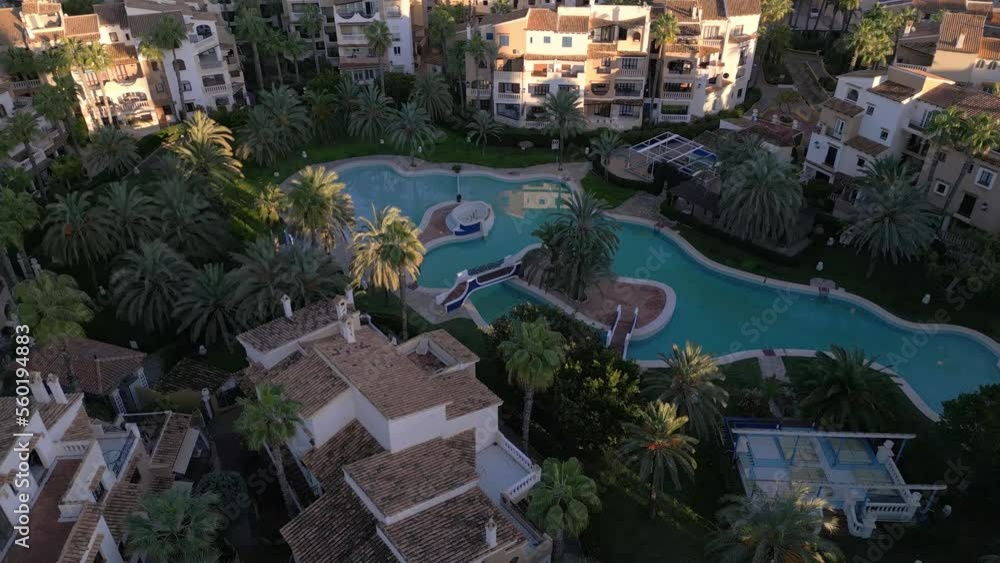 Top-down aerial view of residential neighbourhood showing condos and multi-story buildings with a large public turquoise pool among the palm trees. Torrevieja Spain, sunset time, drone footage Top-down aerial view of residential neighbourhood showing condos and multi-story buildings with a large public turquoise pool among the palm trees. Torrevieja Spain, sunset time, drone footage