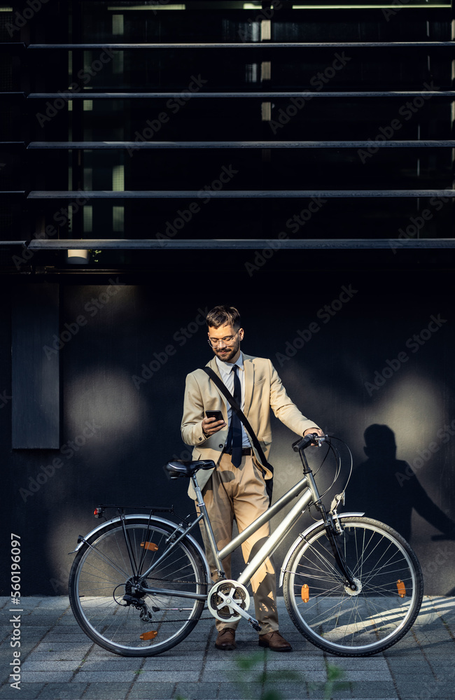 Portrait of business man with bicycle standing in front of office building using smartphone. Portrait of business man with bicycle standing in front of office building using smartphone.