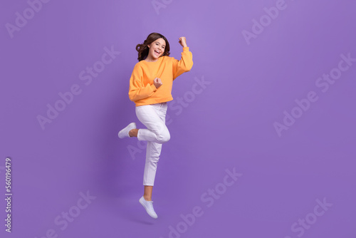 Full size portrait of excited delighted girl jumping raise fists celebrate success empty space isolated on purple color background