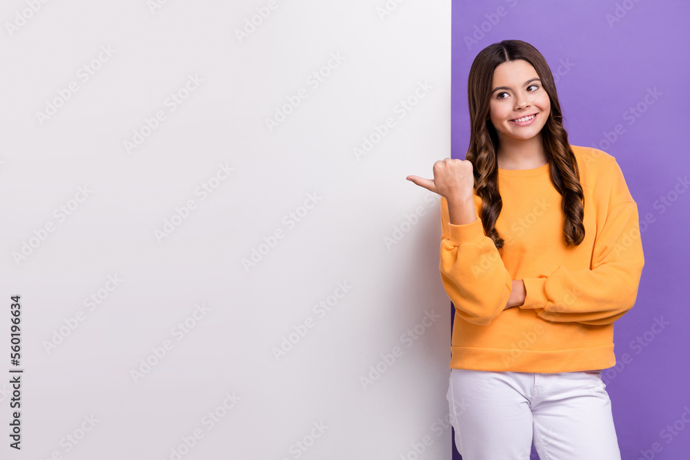 Photo of dreamy cute girl dressed orange sweatshirt looking pointing thumb placard empty space isolated purple color background Photo of dreamy cute girl dressed orange sweatshirt looking pointing thumb placard empty space isolated purple color background