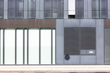 Die Anordnung der Jalousien und Wandelemente eines Gebäudes bilden ein grafisches Muster in weiß, braun und grau. Ein runder Schatten durchbricht die geraden  Konturen.