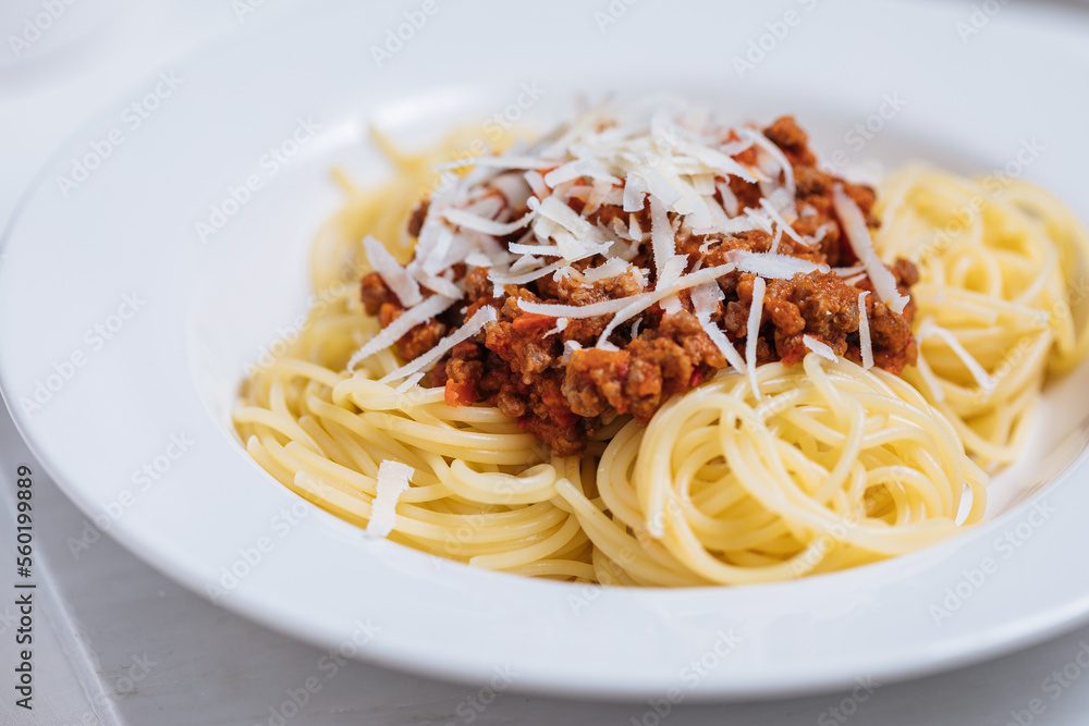 Bolognese spaghetti with parmesan cheese on top in white plate. Simple white background and decoration. Traditional Italian dish, Mediterranean cuisine. 