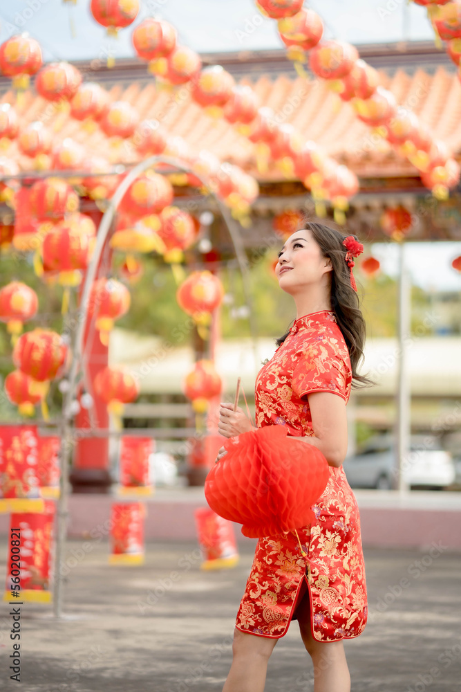 Vertical picture. Happy Asian woman wearing traditional cheongsam qipao dress holding lantern while visiting the Chinese Buddhist temple. Celebrate Chinese lunar new year.
