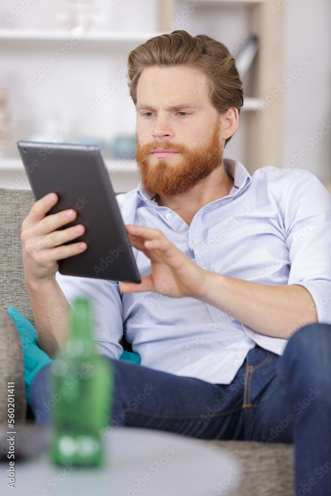 young man with tablet on sofa relaxing at home - obrazy, fototapety, plakaty 