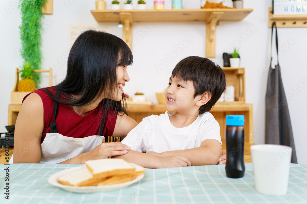 Happy little young boy and his mother making an easy breakfast together in a kitchen with a breads and chocolate jam. Mother and son playing together while making a breakfast. Happy little young boy and his mother making an easy breakfast together in a kitchen with a breads and chocolate jam. Mother and son playing together while making a breakfast.