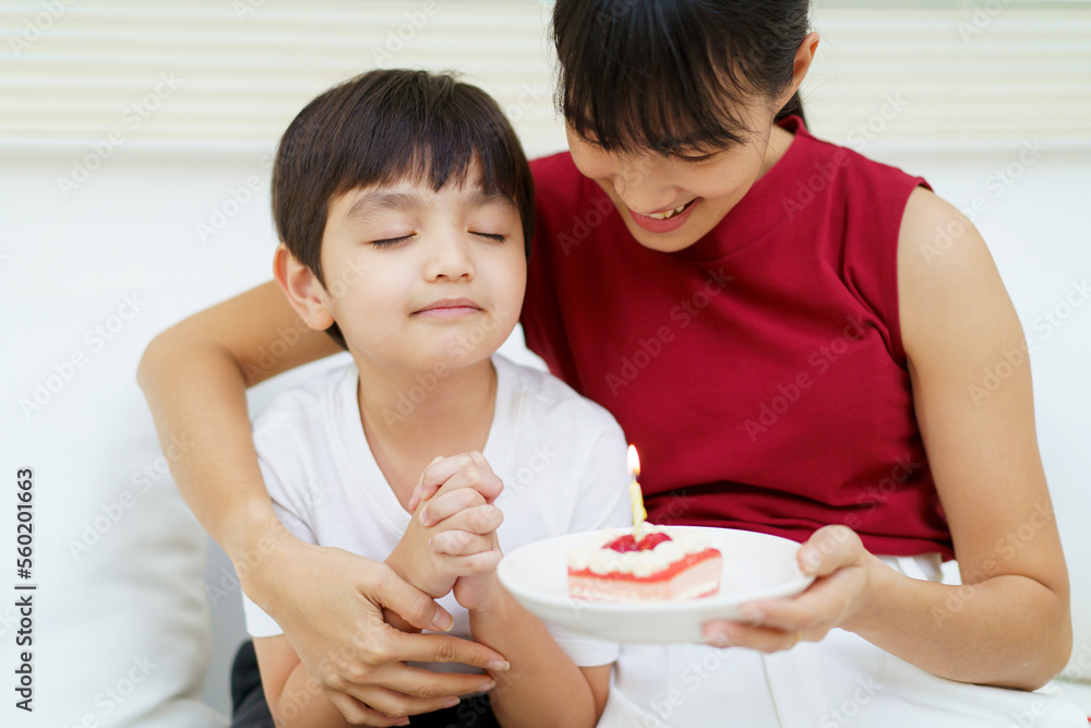 Happy cheerful Asian woman celebrating a birthday with a birthday cake for little young boy and the boy praying before blowing a candle. Happy cheerful Asian woman celebrating a birthday with a birthday cake for little young boy and the boy praying before blowing a candle.