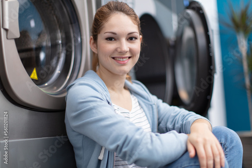 Slika na platnu smiling young woman sitting on floor at launderette