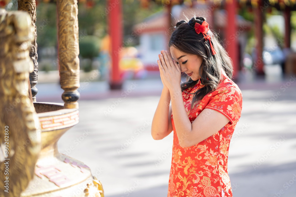 A Young asian woman wearing traditional cheongsam qipao costume praying for best wish blessing and good luck in Chinese Buddhist temple.