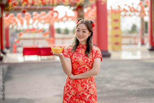 Happy Chinese new year. Asian woman wearing traditional cheongsam qipao dress holding and looking to ancient gold money in Chinese Buddhist temple. Celebrate Chinese lunar new year