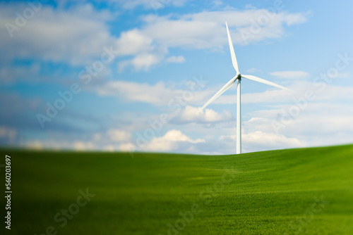 Wind turbines on green farming fields with blue sky and puffy clouds.