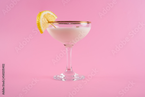 freshly prepared and poured Tuxedo cocktail with a lemon slice on a coctail stick isolated on a pink background