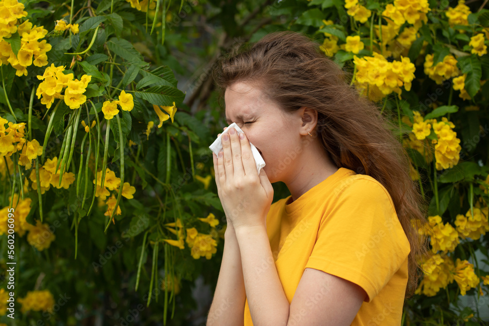 Portrait of beautiful young allergic woman is suffering from pollen allergy or cold on natural flower flowering tree background at spring or sunny summer day sneezes, blowing her runny nose rubs eyes Portrait of beautiful young allergic woman is suffering from pollen allergy or cold on natural flower flowering tree background at spring or sunny summer day sneezes, blowing her runny nose rubs eyes