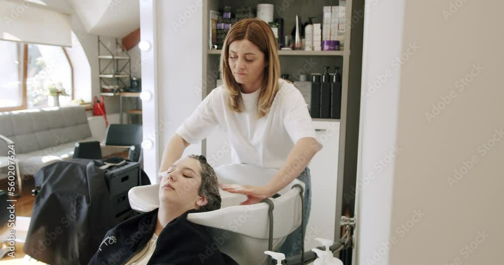 Washing hair and head massage in beauty salon before female haircut. Hairstylist washing hair with shampoo in hairdressing salon. Young woman in beauty studio. Treatment and care in spa. Washing hair and head massage in beauty salon before female haircut. Hairstylist washing hair with shampoo in hairdressing salon. Young woman in beauty studio. Treatment and care in spa.