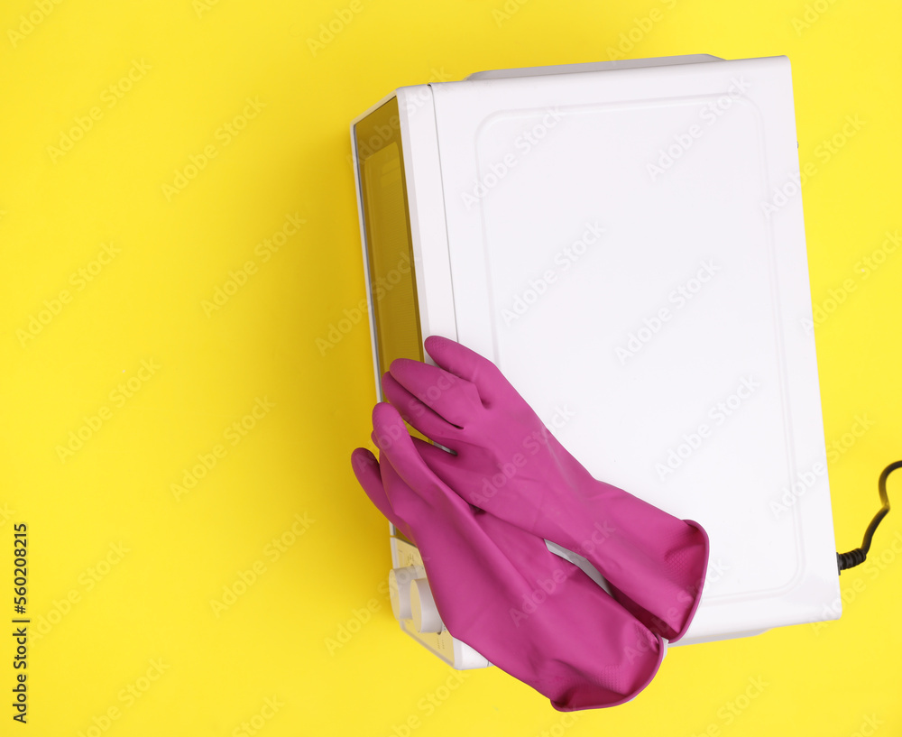 Microwave with cleaning gloves on yellow background. Kitchen cleaning concept. Top view Microwave with cleaning gloves on yellow background. Kitchen cleaning concept. Top view