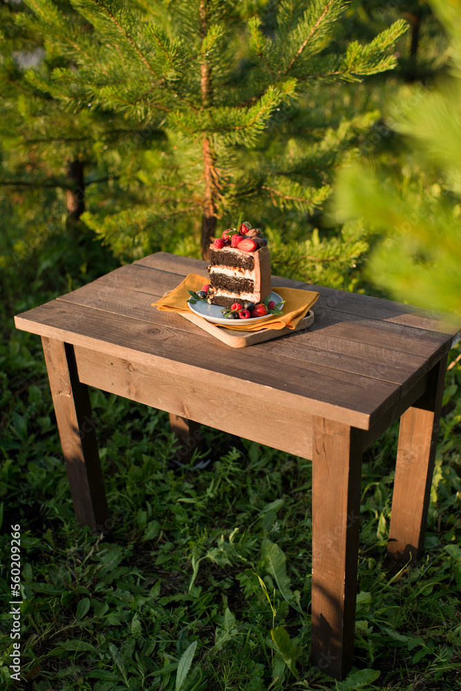 An appetizing piece of cake decorated with berries stands on a wooden table in nature