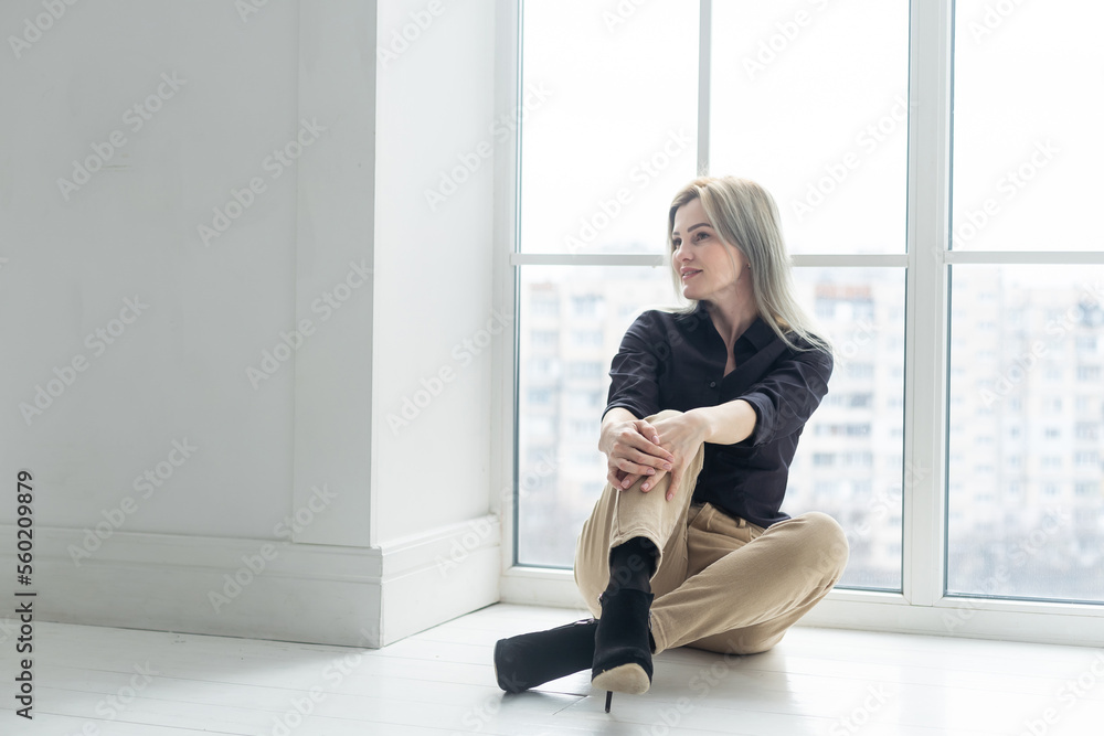 Side view of young businesswoman in white shirt sitting on floor near window Side view of young businesswoman in white shirt sitting on floor near window