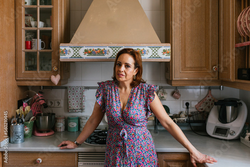 Woman looking at camera while standing in the kitchen at home.