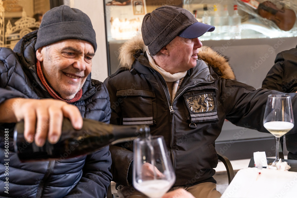 two elegant mature men in hats toasting with white wine on an outdoor street two elegant mature men in hats toasting with white wine on an outdoor street
