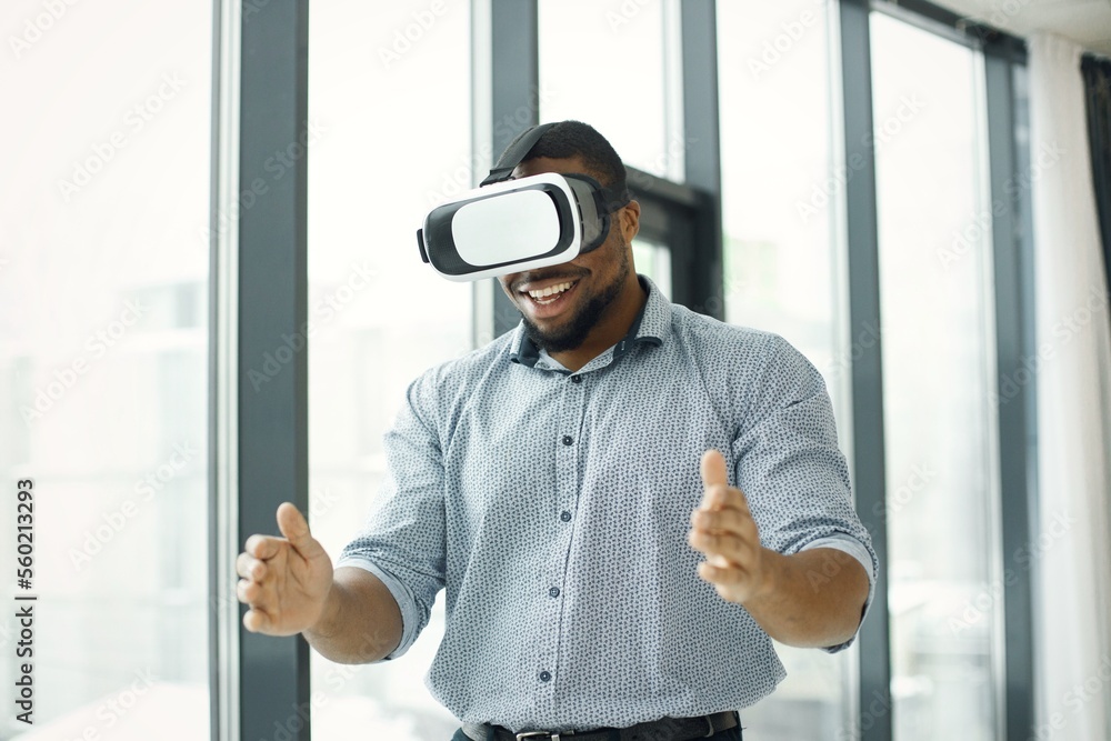 Black male entrepreneur standing near big windows wearing virtual reality glasses