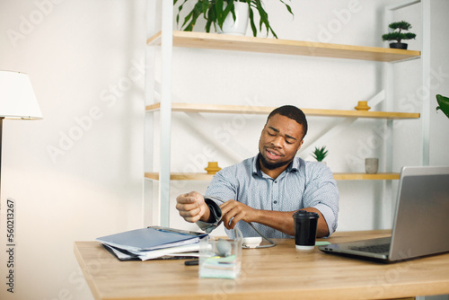 Black male entrepreneur sitting in office near laptop and using tonometr