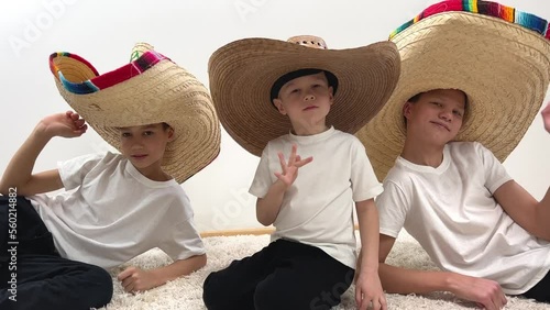 children three boys in mexican hats and white t-shirts waving their hands at camera straw hats with a rim on a white background photo