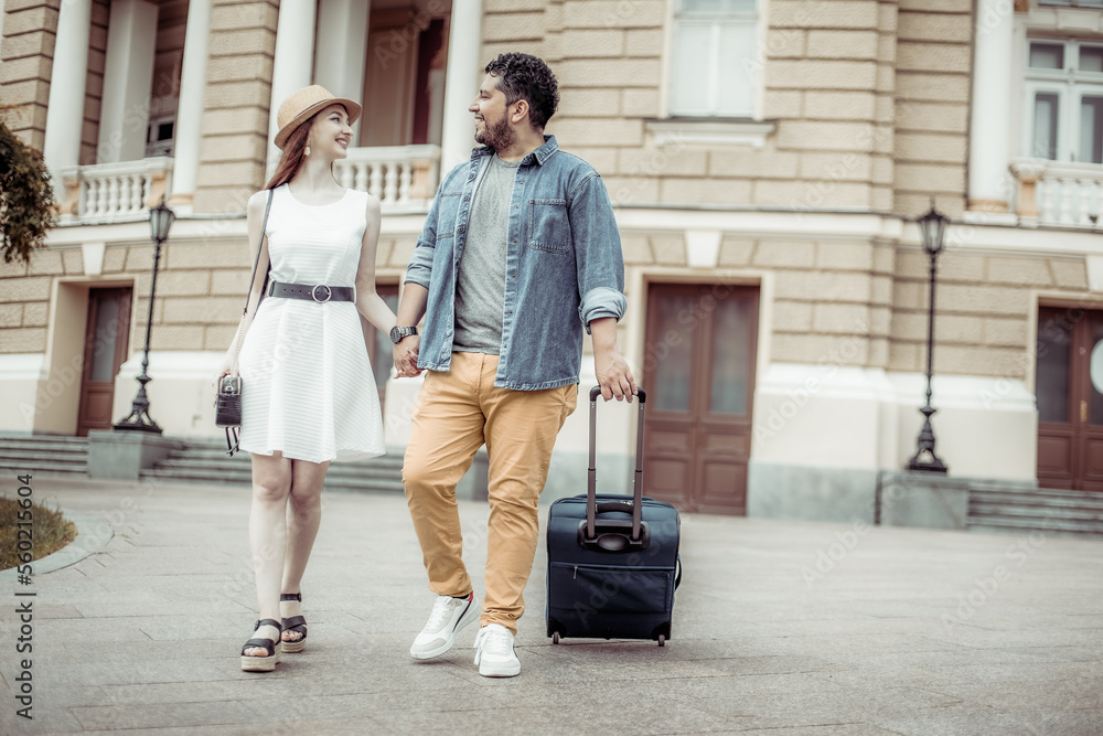 International couple of tourists walking along a European street with travel luggage