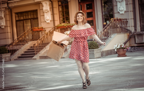 Beautiful emotional woman shopaholic in red polka dot dress with shopping packages in the city