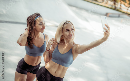 Two beautiful athletic women take selfie on smartphone outdoors