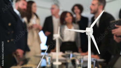 Close-up wind turbine gadget. Background with businesspeople in meeting. Sustainable energy project.